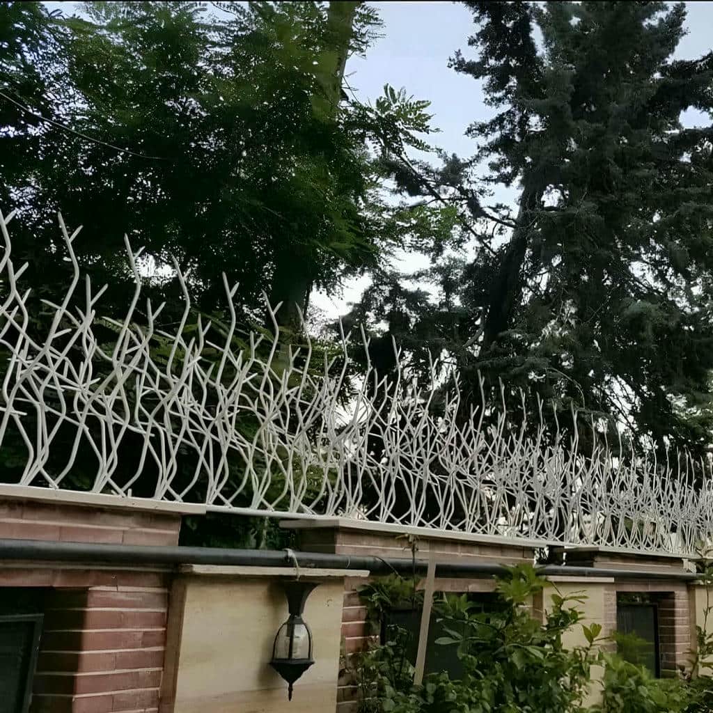 نرده سرنیزه‌ای خاکستری روی دیوار بلوکی حیاط